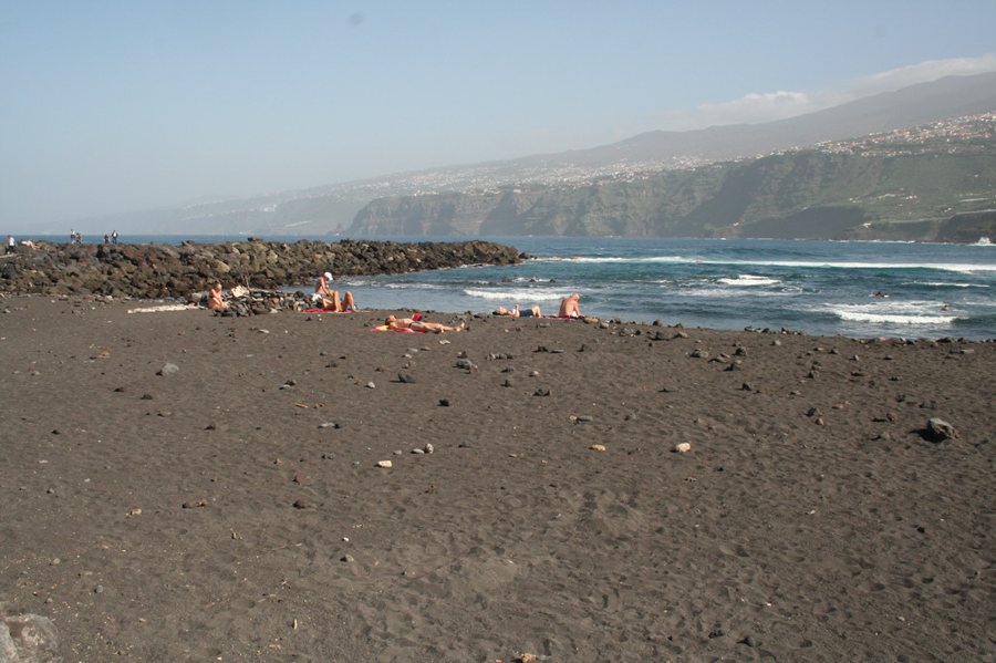 Dunkler Sandstrand mit Wellen und steinigem Wellenbrecher an Teneriffas Nordküste